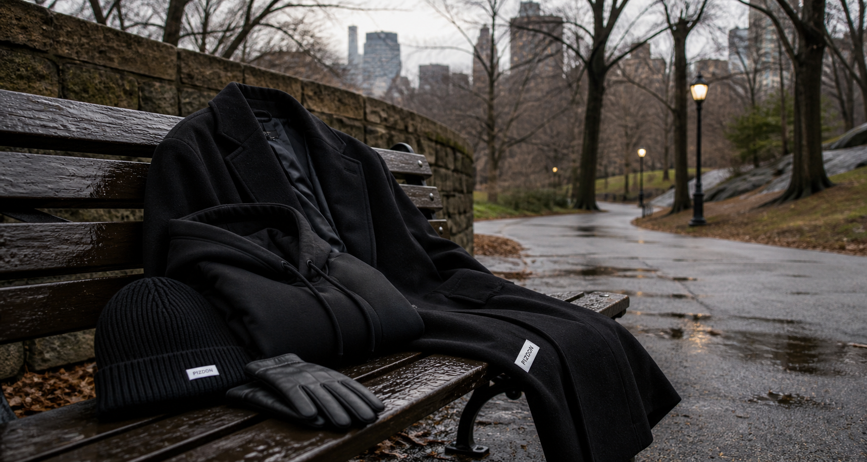 PIZDON black outerwear, hoodie, beanie, and gloves on a wet Central Park bench